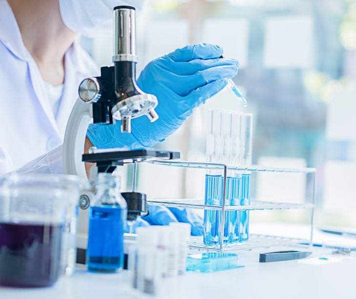 person in research lab with microscope and test vials