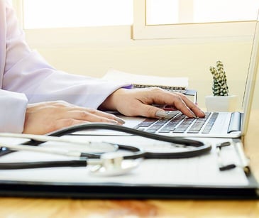 hands at computer with stethoscope on desk