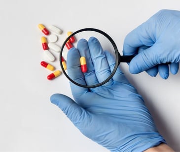 gloved hand holding pill and magnifying glass