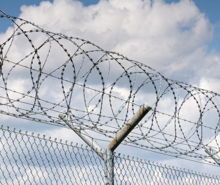 Image of barbed wire on top of a fence. 