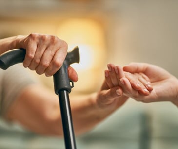 Image of individual helping another individual with a cane. 